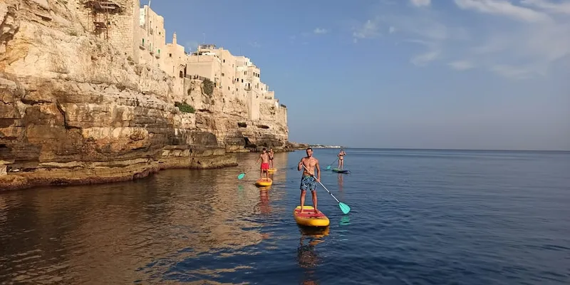 Stand-up paddle sous les falaises de Polignano a Mare au ras de l'eau, mai, Pouilles