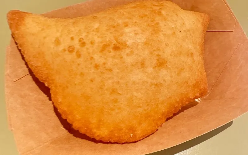 Panzerotto fritto doré tenu à la main dans une ruelle de Bari Vecchia, street food traditionnel des Pouilles