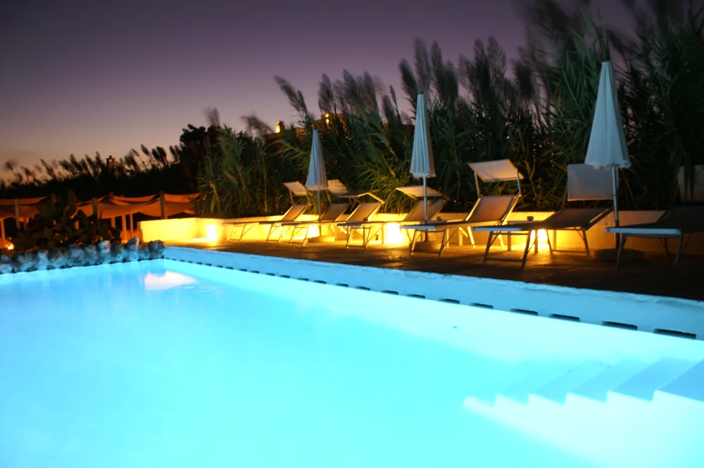 Piscine illuminée au bord d'une masseria dans la plaine des oliviers millénaires au coucher du soleil, Pouilles, Italie