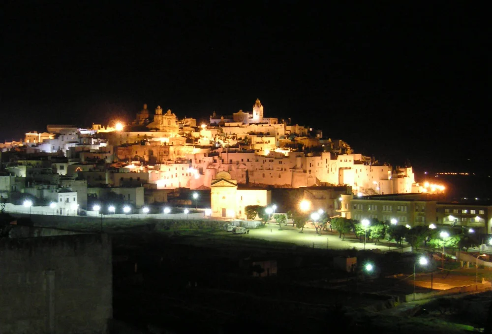 Ruelles illuminées d'Ostuni la nuit, façades blanches baignées par les lampadaires en fer forgé couleur miel, Pouilles
