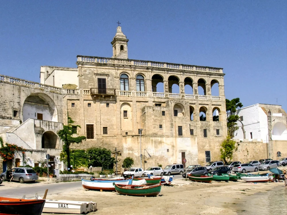 Abbaye bénédictine de San Vito se reflétant dans l'eau claire de la crique, petit port de pêche au premier plan, côte nord de Polignano a Mare