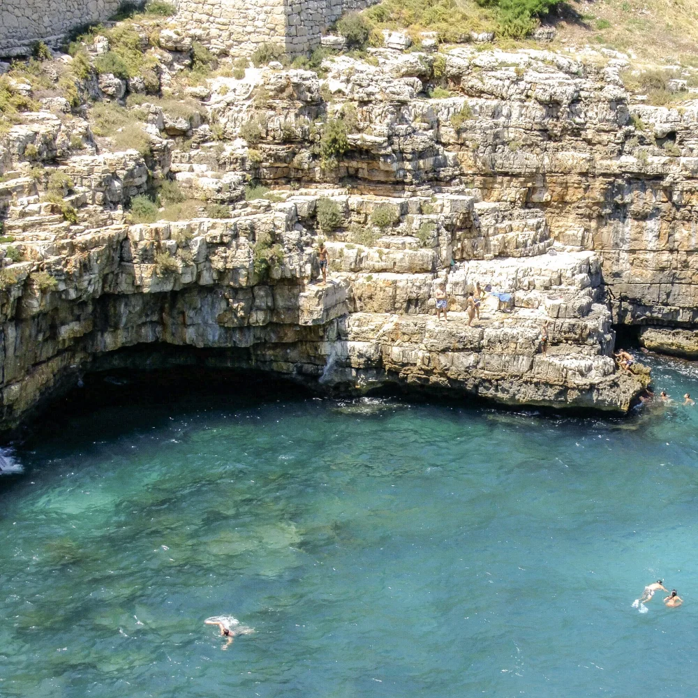 Embarcation traditionnelle gozzo naviguant à l'entrée d'une grotte marine de Polignano a Mare, lumière bleue sous-marine, Pouilles