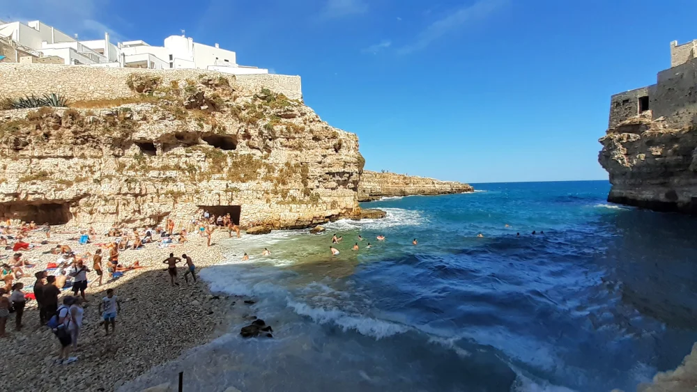 Crique de galets de Lama Monachile encadrée par les hautes falaises calcaires de Polignano a Mare avec le pont romain en arrière-plan, mer Adriatique, Pouilles