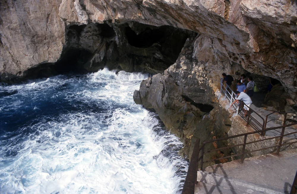 Entrée de la Grotte de Neptune au Capo Caccia, falaises calcaires plongeant dans la mer bleue de Sardaigne