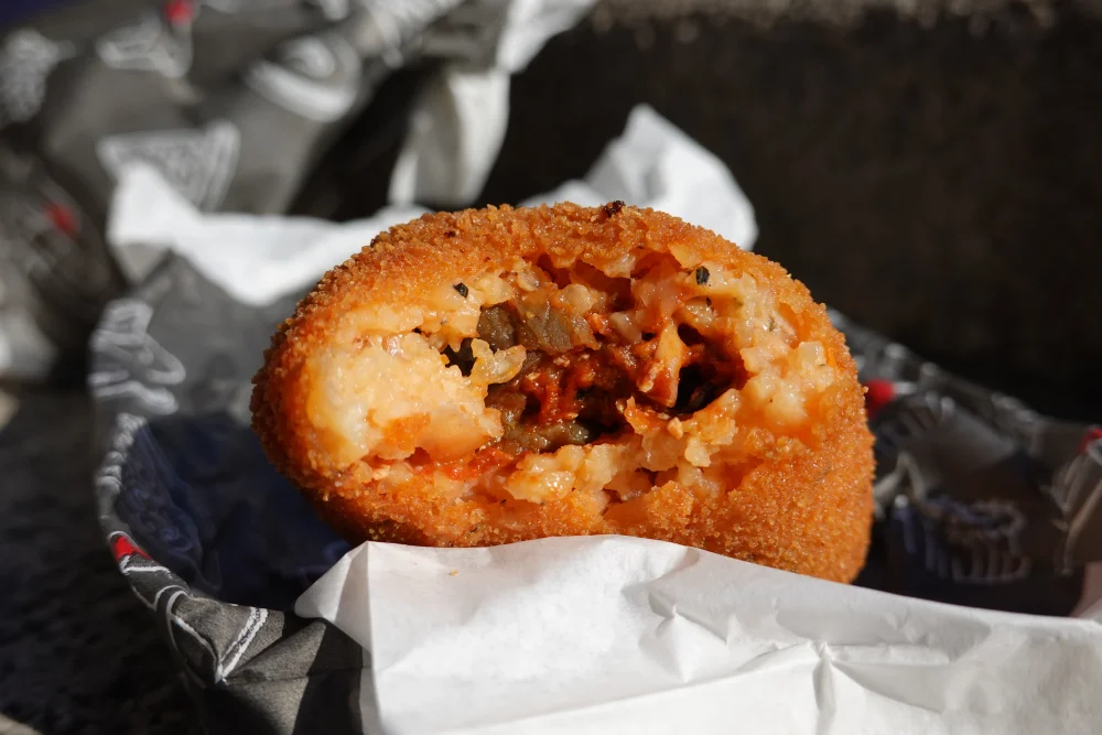 Arancino sicilien pointu tenu à la main, street food traditionnelle de Catane, Sicile
