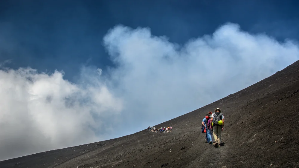 Randonneurs en tenue de montagne sur les pentes volcaniques de l'Etna, terrain de cendres et scories