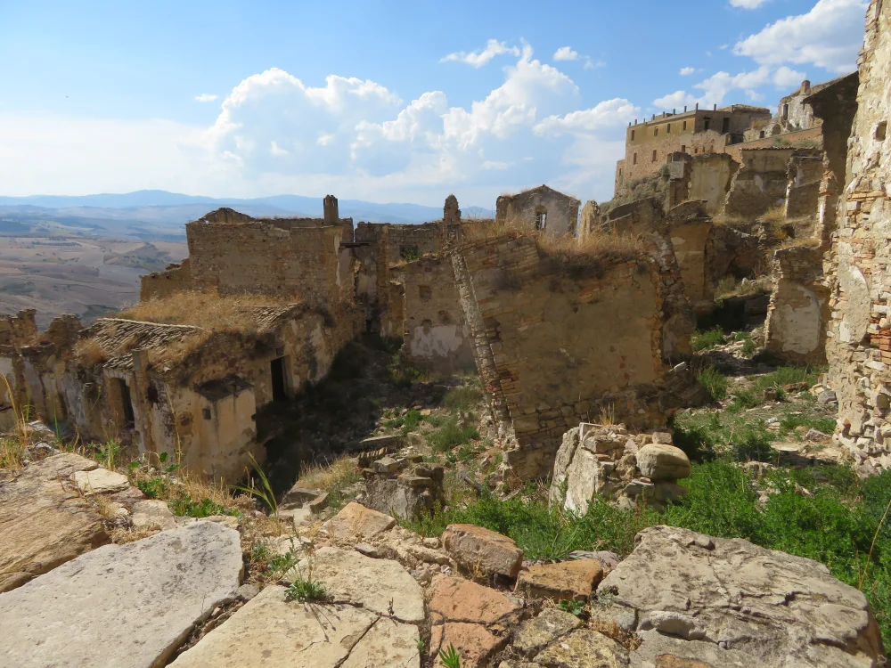 Ruines de Craco sous un ciel bleu éclatant, façades de pierre effondrées, Basilicate