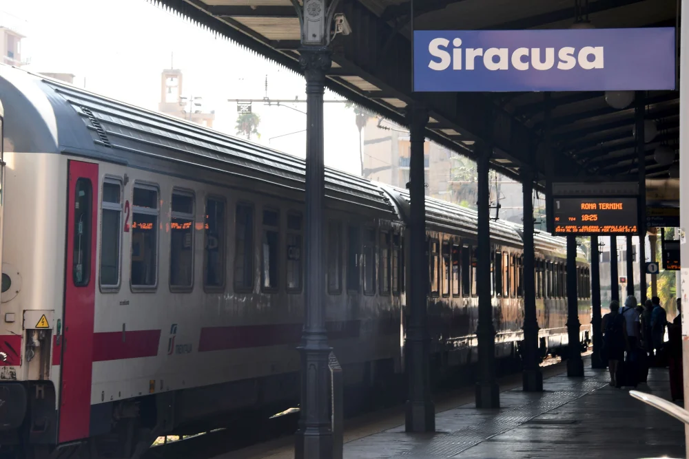 Train régional Trenitalia longeant la côte sicilienne, vagues se brisant sur les rochers au lever du jour